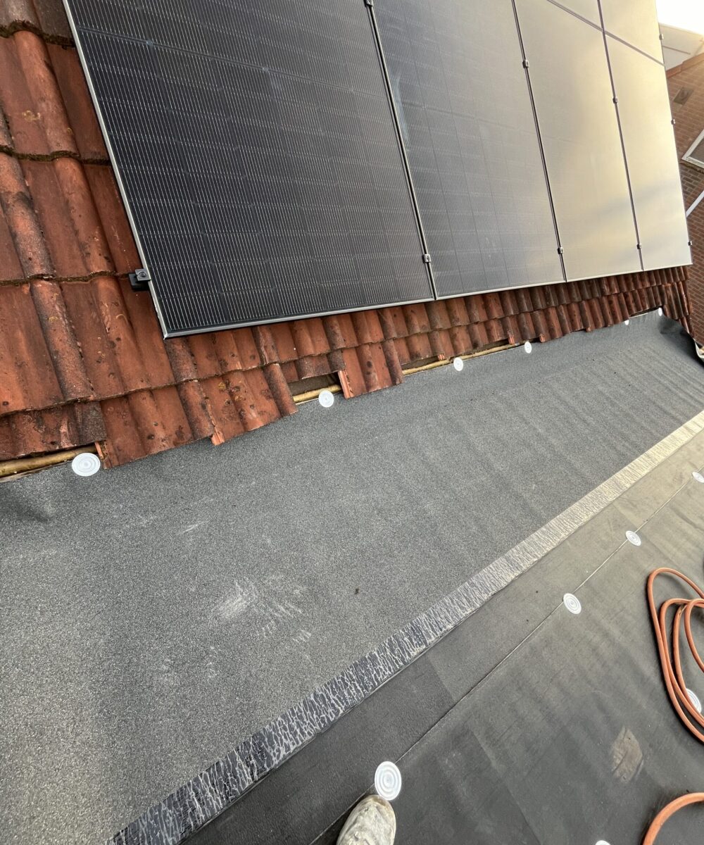 Dakaanzicht met geïnstalleerde zonnepanelen en dakbedekkingsmaterialen, waaronder teerpapier en dakpannen. Een voet gedeeltelijk zichtbaar op de voorgrond. Dakaanzicht met geïnstalleerde zonnepanelen en dakbedekkingsmaterialen, waaronder teerpapier en dakpannen. Een voet gedeeltelijk zichtbaar op de voorgrond.