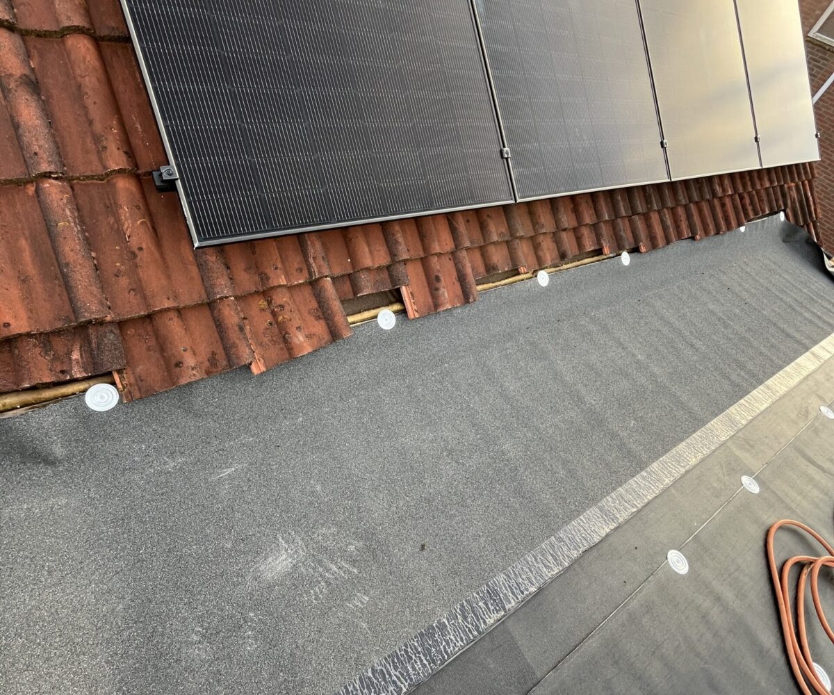 Dakaanzicht met geïnstalleerde zonnepanelen en dakbedekkingsmaterialen, waaronder teerpapier en dakpannen. Een voet gedeeltelijk zichtbaar op de voorgrond. Dakaanzicht met geïnstalleerde zonnepanelen en dakbedekkingsmaterialen, waaronder teerpapier en dakpannen. Een voet gedeeltelijk zichtbaar op de voorgrond.