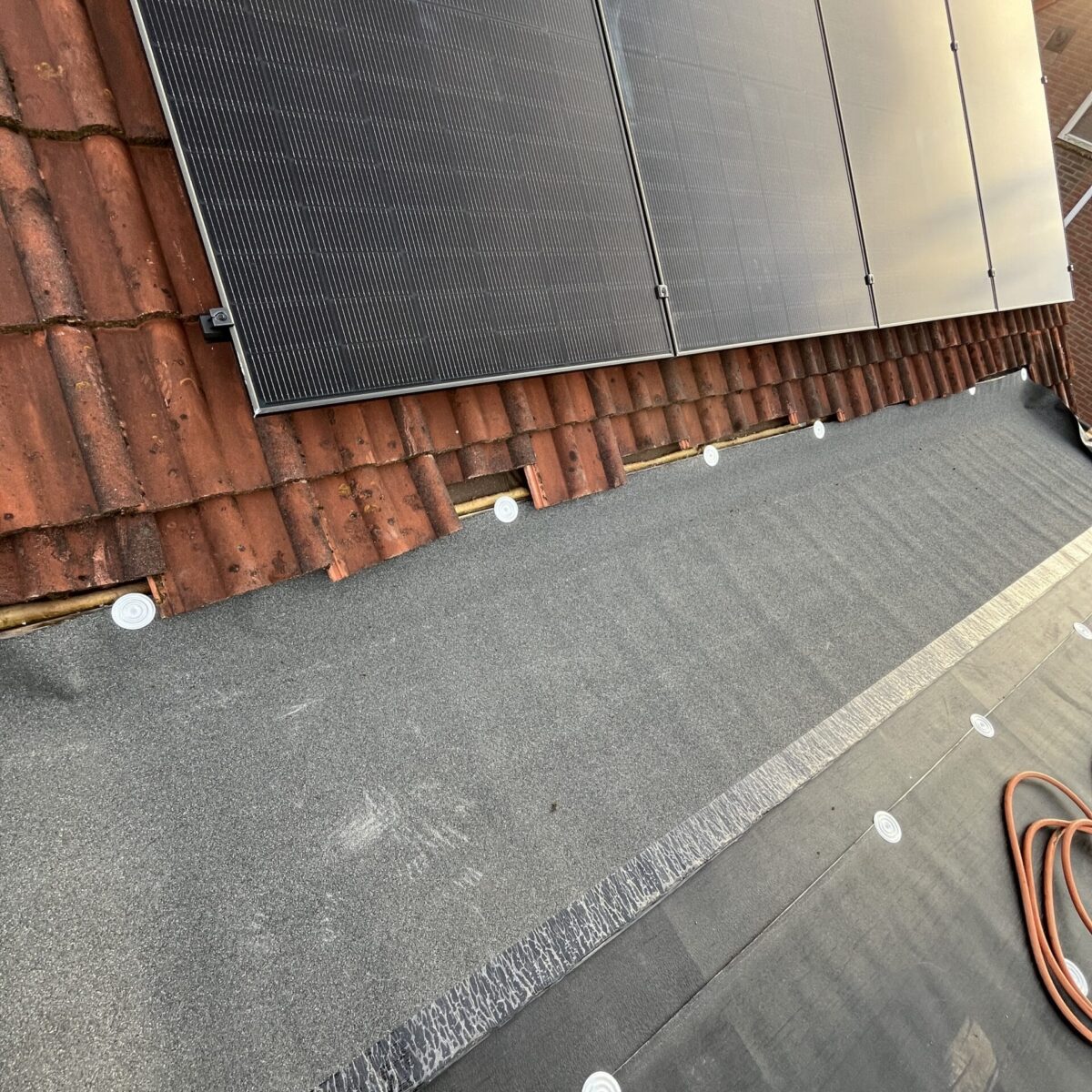 Dakaanzicht met geïnstalleerde zonnepanelen en dakbedekkingsmaterialen, waaronder teerpapier en dakpannen. Een voet gedeeltelijk zichtbaar op de voorgrond. Dakaanzicht met geïnstalleerde zonnepanelen en dakbedekkingsmaterialen, waaronder teerpapier en dakpannen. Een voet gedeeltelijk zichtbaar op de voorgrond.