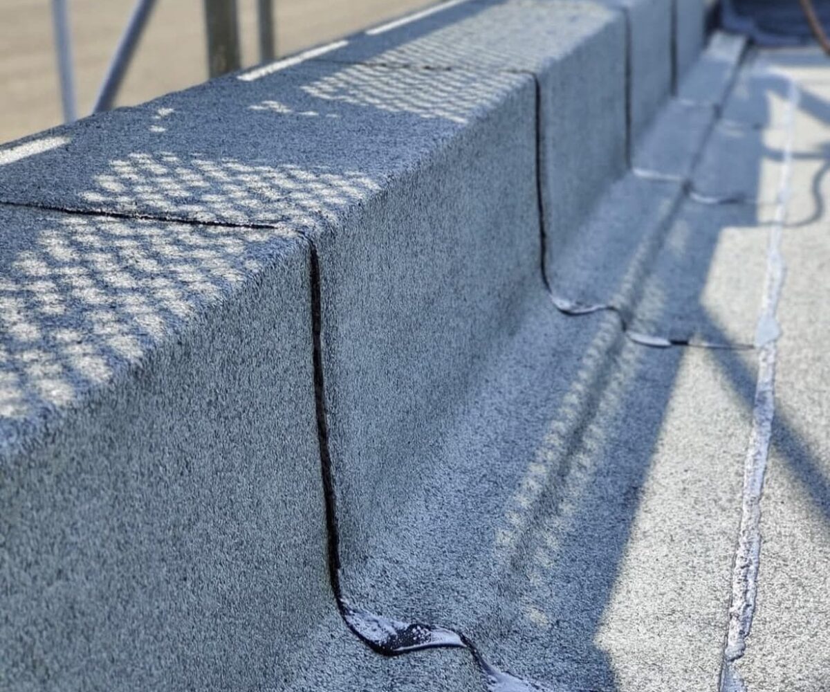 Close-up van een dakhoek tijdens een dakinspectie, met kit aangebracht langs de voegen en naden. Hierdoor zijn het gestructureerde oppervlak en de schaduw van een nabijgelegen structuur goed te zien. Close-up van een dakhoek tijdens een dakinspectie, met kit aangebracht langs de voegen en naden. Hierdoor zijn het gestructureerde oppervlak en de schaduw van een nabijgelegen structuur goed te zien.